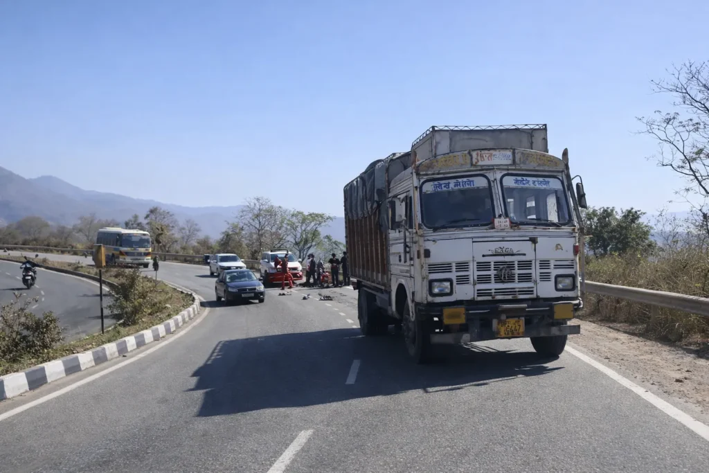 किरतपुर-नेरचौक फोरलेन पर ट्रक और बाइक की टक्कर के बाद सड़क पर खड़ा ट्रक, आसपास मौजूद लोग और राहतकर्मी